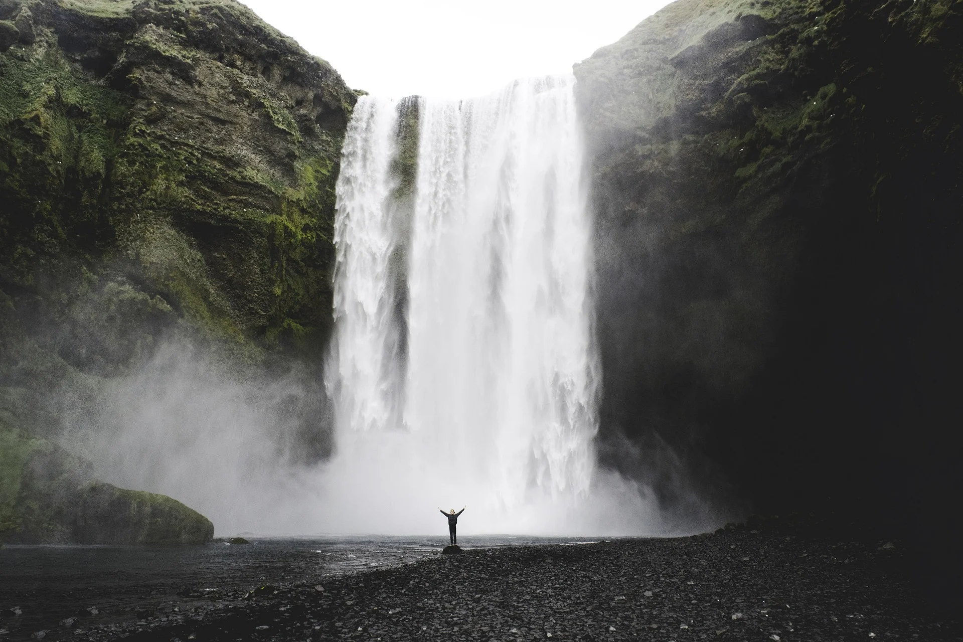 Person standing at the base of large waterfall