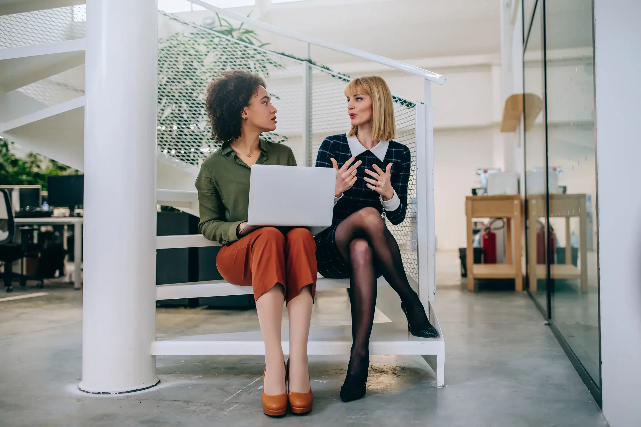 Woman seeking feedback from another woman sitting on spiral staircase